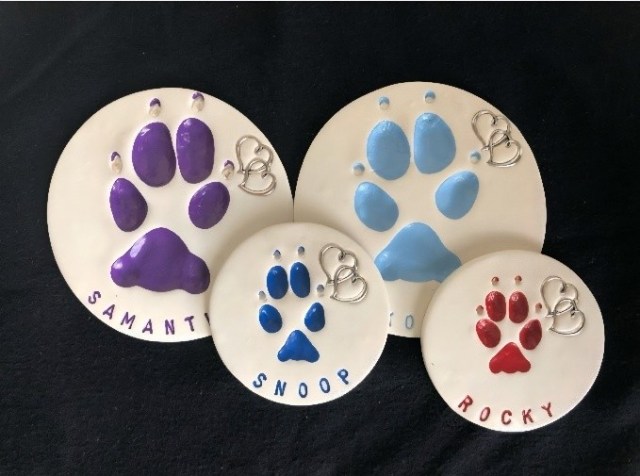 Clay paw print keepsakes in various colors, labeled with names "SAMANTH," "SNOOP," and "ROCKY," representing options for memorializing pets after in-home euthanasia.